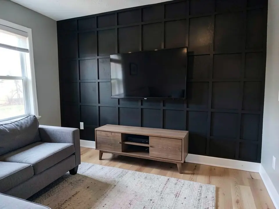 AI-generated edit of the same living room: the TV wall is now covered in a black square grid of trim strips painted the same black as the wall; TV, console, sofa, rug, floor and the other walls unchanged