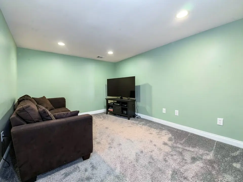 The same basement with the walls painted soft green, with the baseboards, sofa, TV and ceiling kept