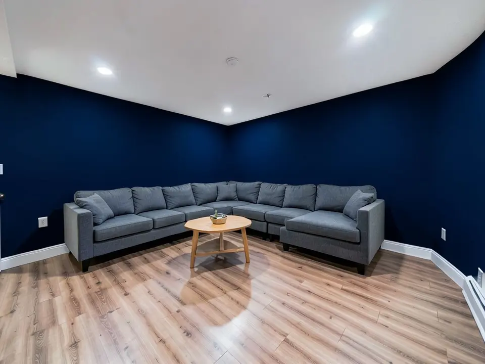 The same basement with the walls painted deep navy, with the sofa, table, baseboards and ceiling kept