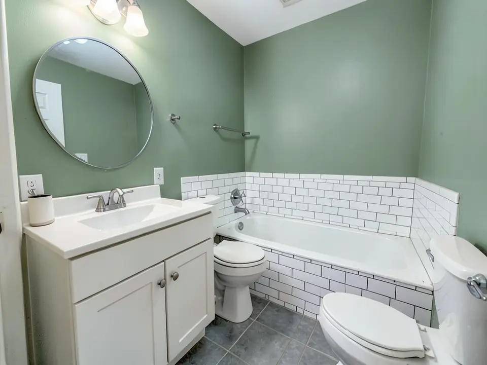 The same bathroom with the painted walls changed to a green, with the white vanity, tile and tub kept