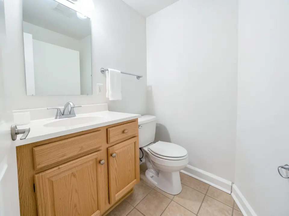 Bathroom with white painted walls, a light oak vanity with a white countertop, a rectangular mirror, a white towel and a beige tile floor, before