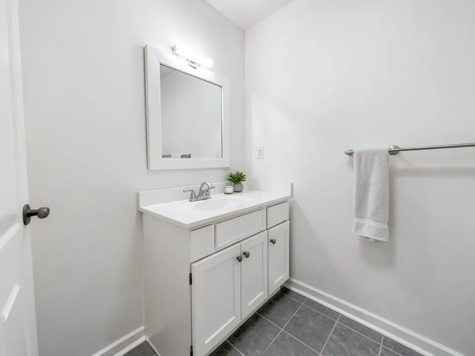 Bathroom with white walls, a white vanity and sink, a framed mirror, a towel and gray tile, before