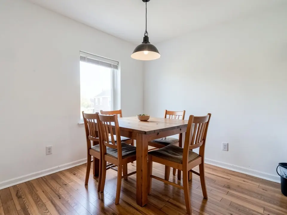 Dining room with white walls, a wooden table with chairs, a black pendant light and a window, before