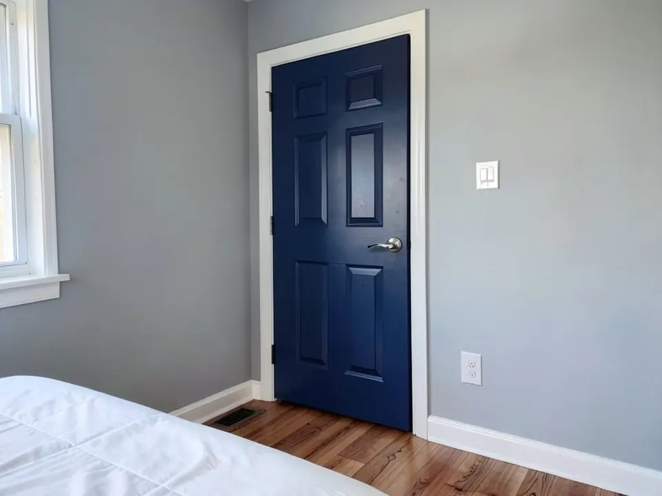 The same room with the six-panel door painted deep navy, with the light gray walls and white casing kept