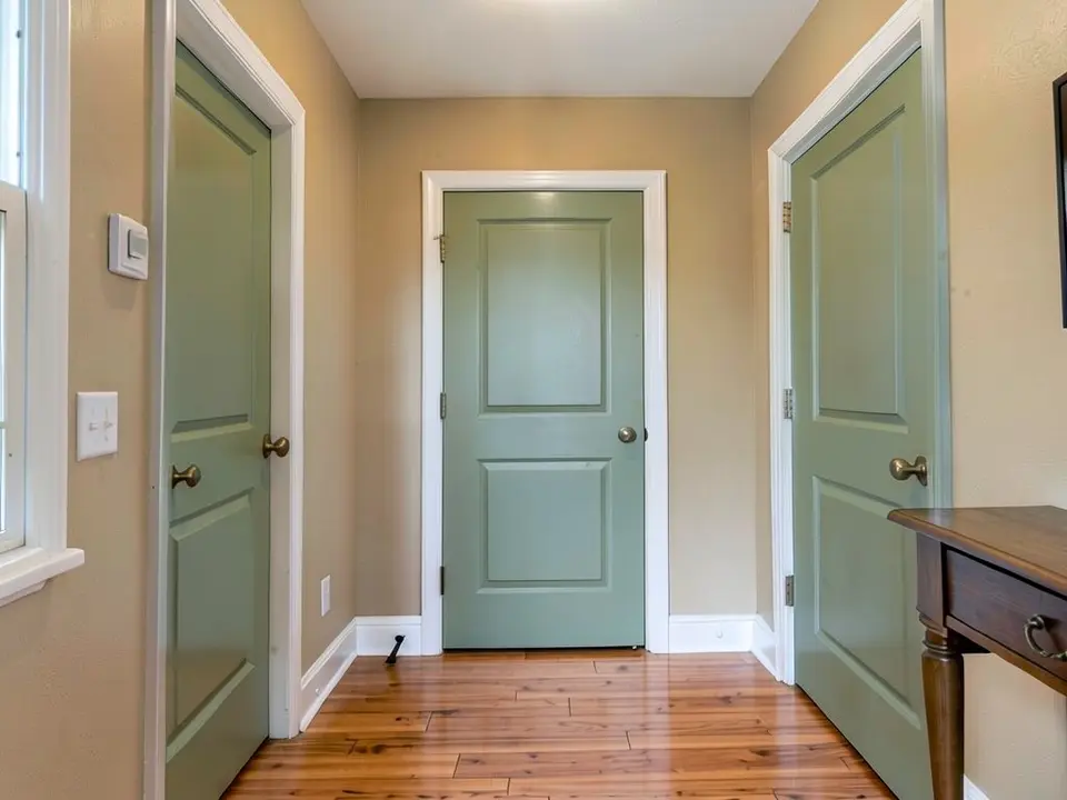 The same hallway with the three paneled doors painted a muted sage green, with the beige walls and white casings kept