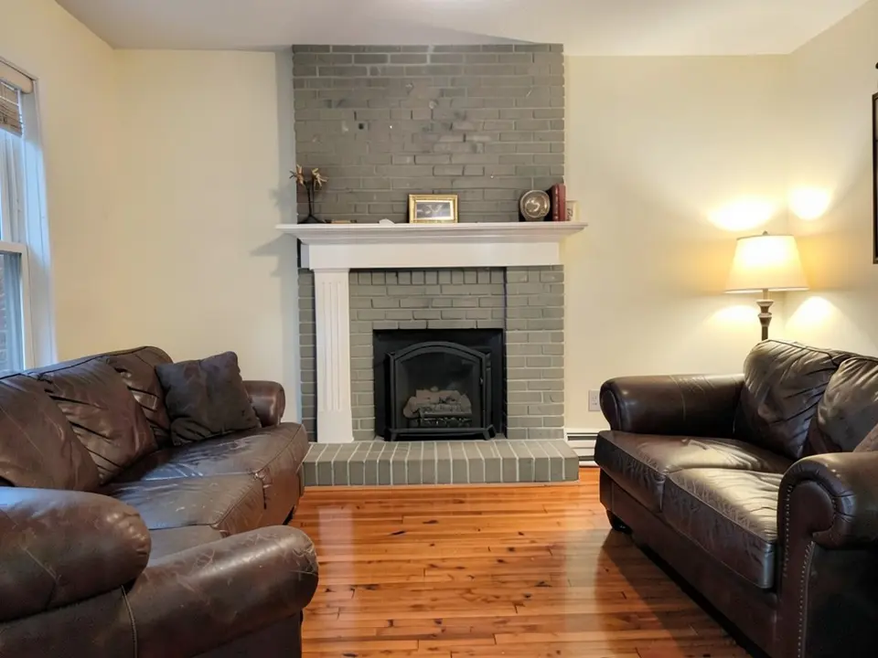 The same room with the dark red brick fireplace and hearth painted a gray-green, with the white mantel kept