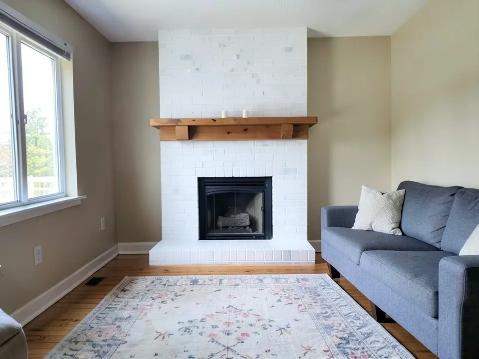 The same room with the brick fireplace and hearth painted white, with the wooden mantel kept