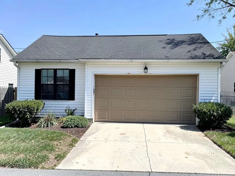 White vinyl siding ranch house with black shutters and an almond raised panel garage door, before