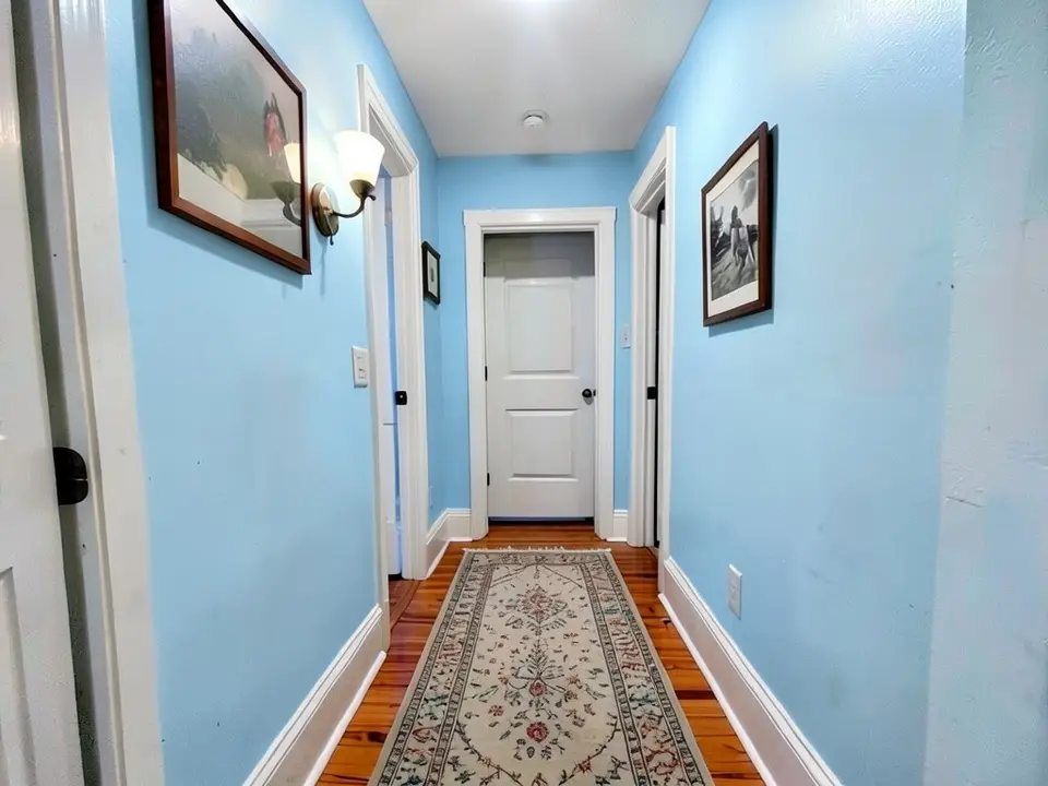 The same hallway with the walls painted light blue, with the trim, doors, pictures, sconce and floor kept