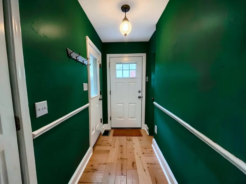 The same entry hall with the walls painted deep emerald green, with the chair rail, door, hooks and pendant light kept