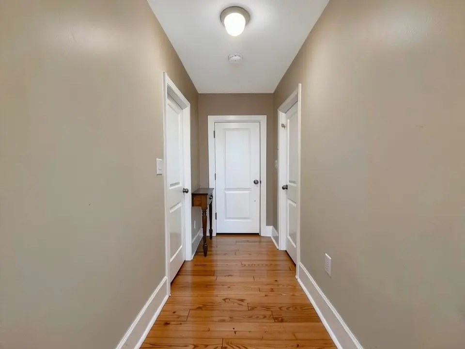 The same hallway with the walls painted warm taupe, with the doors, trim, table and floor kept