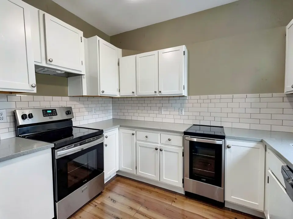 The same kitchen with the walls painted a warm greige, with the white cabinets, countertop, backsplash, range and floor kept