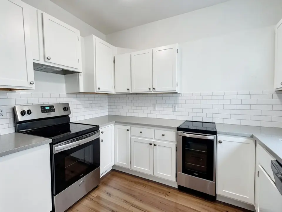 Kitchen with stark white walls, white shaker cabinets, a gray countertop, a white subway tile backsplash, a stainless range and a wood floor, before