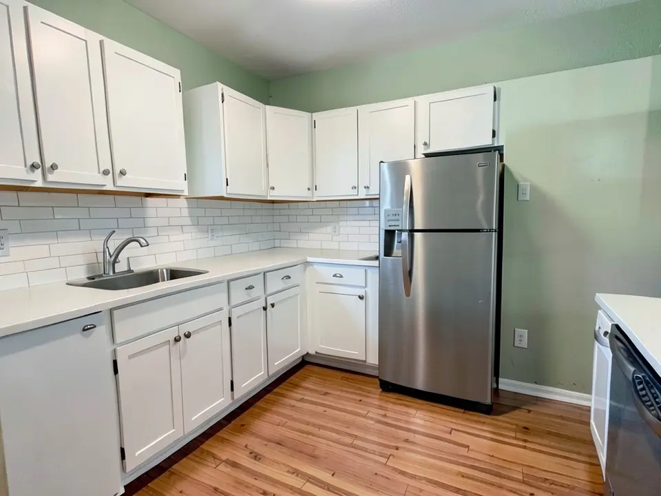 The same kitchen with the walls painted a soft sage green, with the cabinets, countertop, backsplash, fridge and floor kept