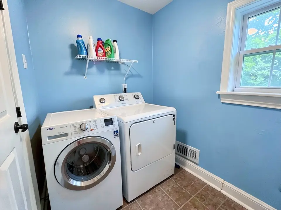 The same laundry room with the walls painted bright blue, with the window, shelf, bottles and machines kept