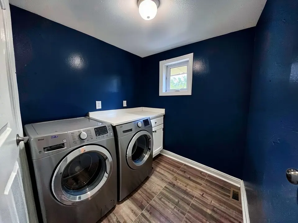 The same laundry room with the walls and the foreground door painted deep navy, with the countertop, window and machines kept