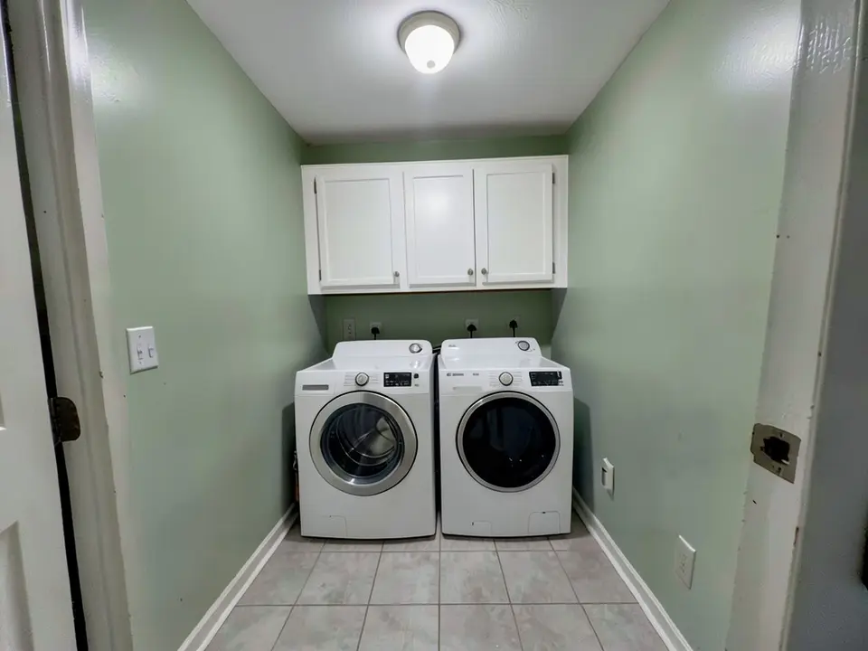 The same laundry room with the walls painted pale green, with the cabinets, machines and ceiling light kept