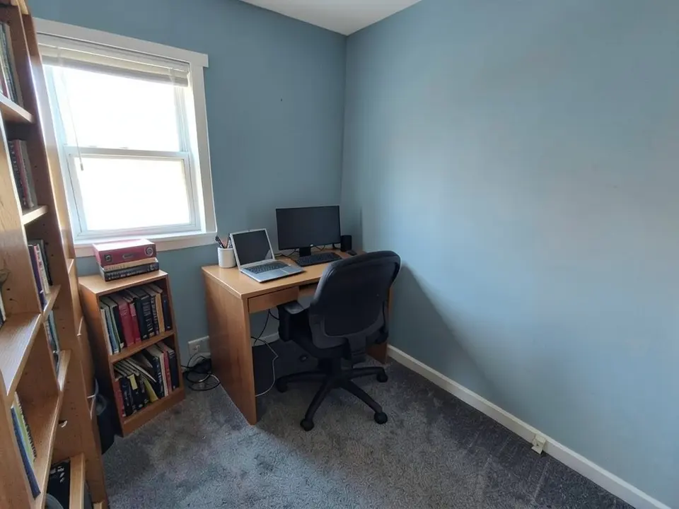 The same home office with the walls painted dusty blue, with the desk, chair, bookshelves and window kept