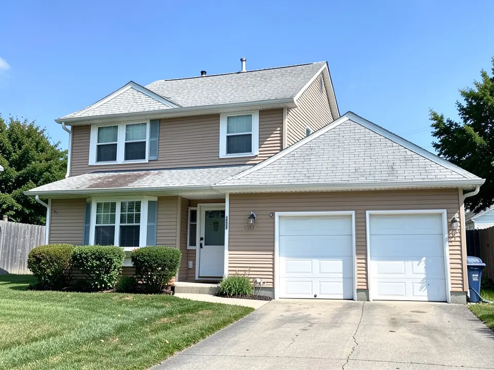Two-story house with tan vinyl siding, white trim, a worn light gray shingle roof with dark stains and a two-car garage, before