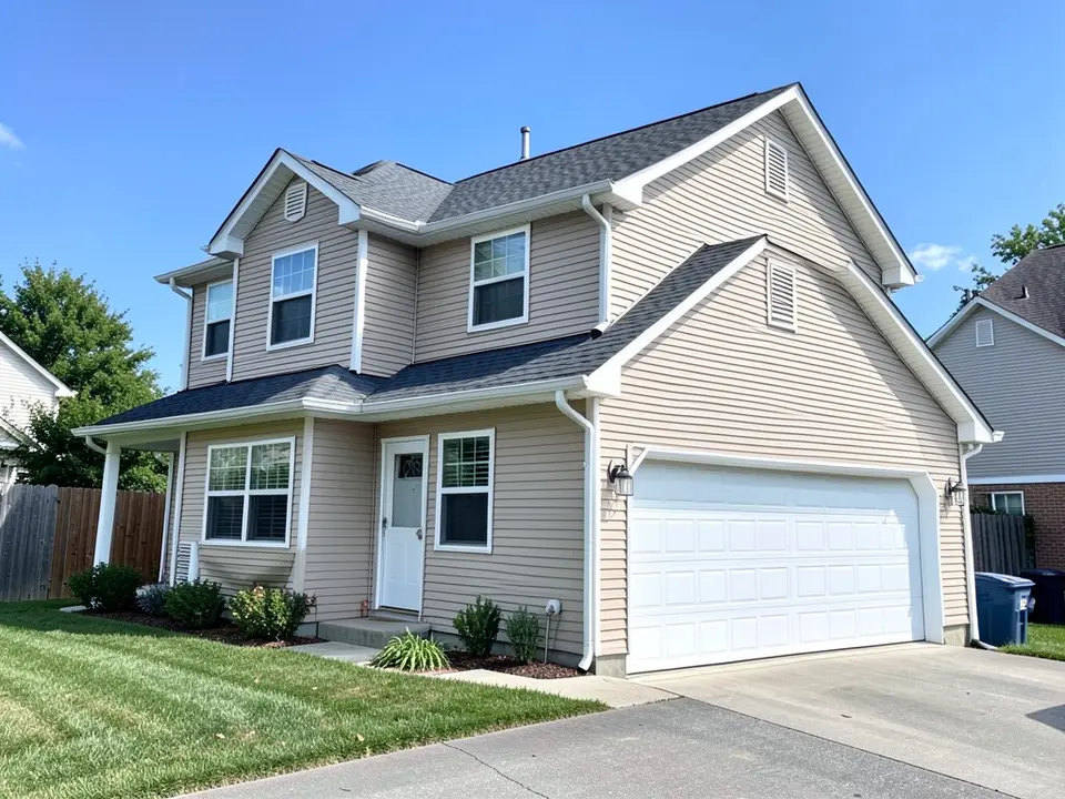Two-story suburban house with beige vinyl lap siding, white window trim and corner boards, a dark gray shingle roof and a white two-car garage door, before