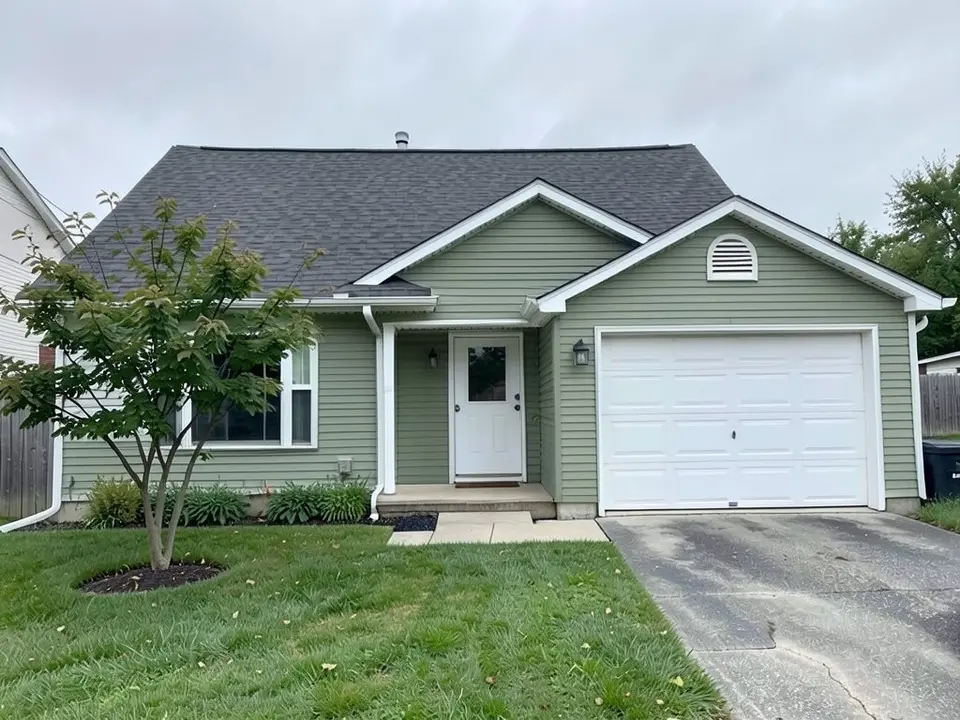 The same house with the siding painted muted sage green and the garage door left white