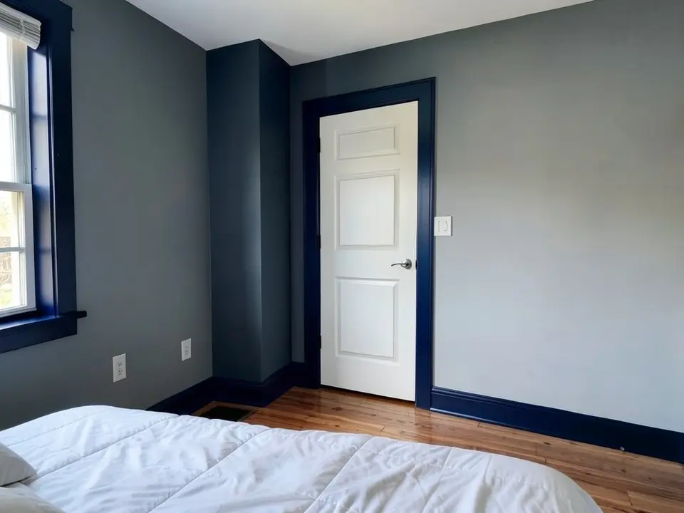 The same bedroom with the baseboards, door casing and window frame painted navy while the door stays white
