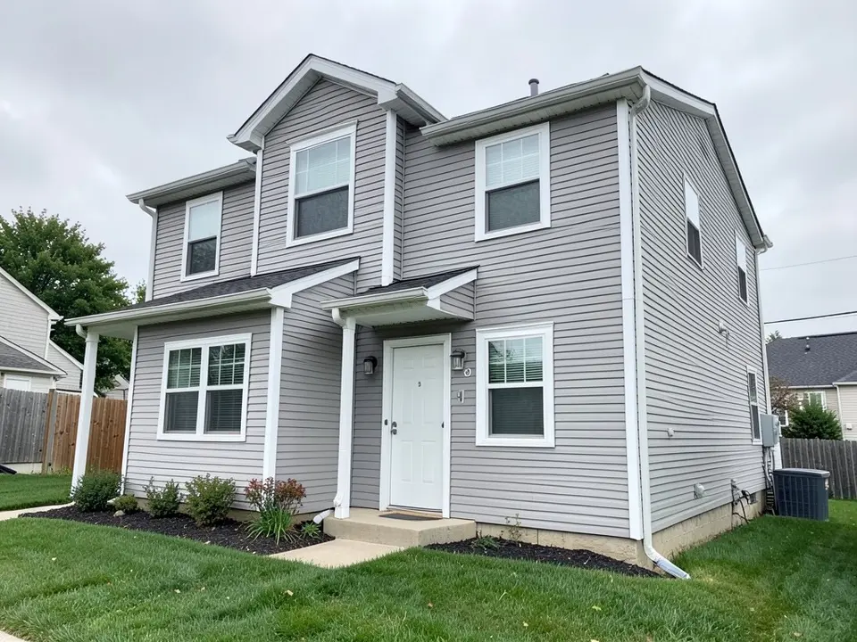 Two-story house with light gray vinyl siding and white window trim, corner boards and door trim, before