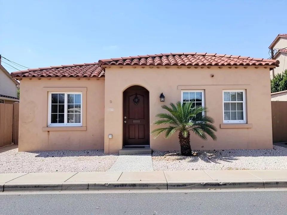 Single-story Spanish style house with peach-beige stucco walls, red clay tile roof and an arched wooden front door, before